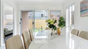 A modern dining area with a marble table, beige chairs, and a view of the backyard through a glass door.