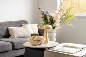 Una sala de estar moderna con un sofá gris, una mesa redonda con una lámpara, una planta decorativa y una revista.