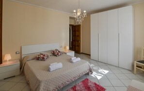 Una habitación de hotel con cama, mesitas de noche, una araña, un armario y una alfombra roja.