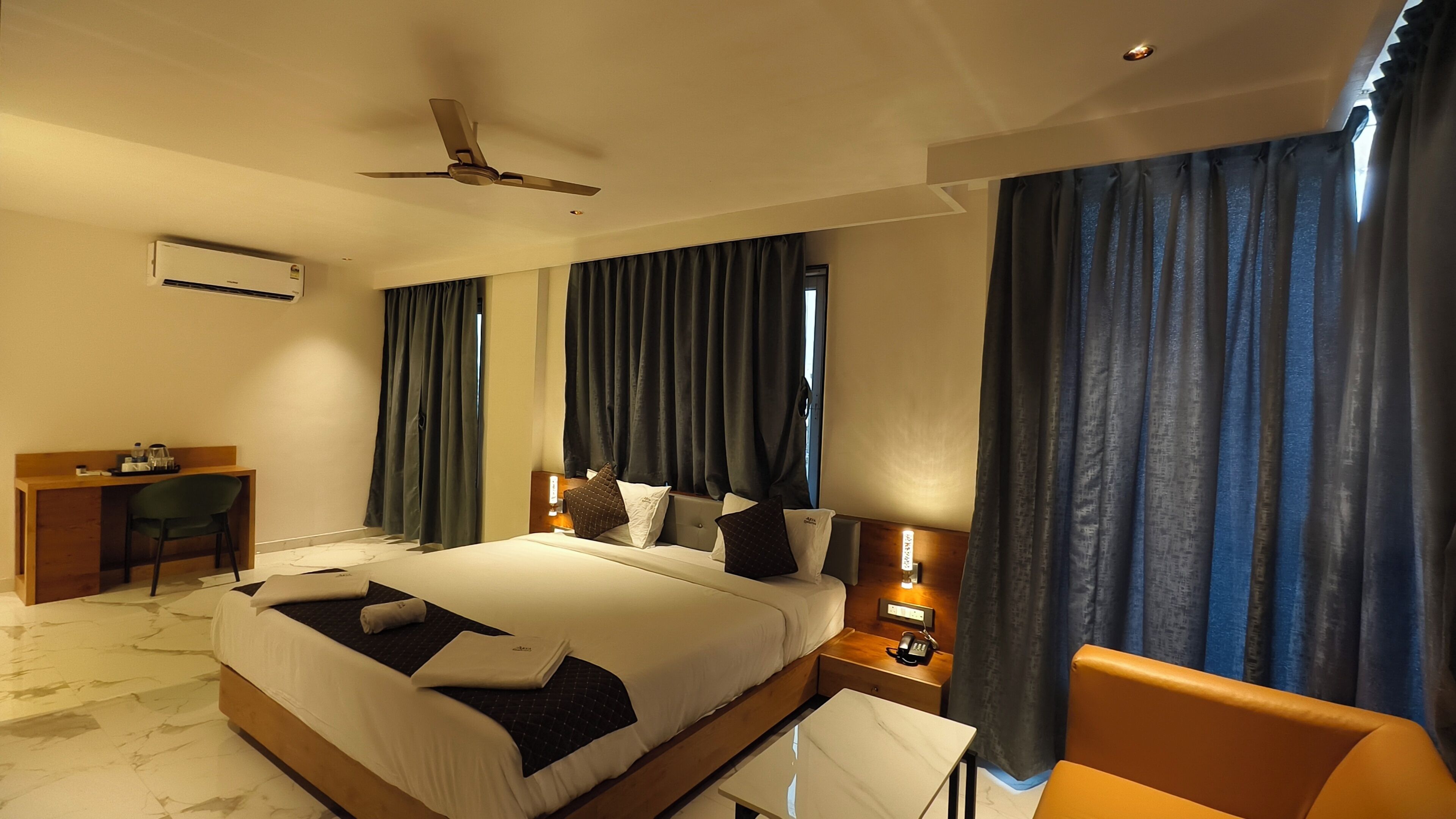 Habitación de hotel con una cama grande, un escritorio, una silla, una mesita de noche y un ventilador de techo.