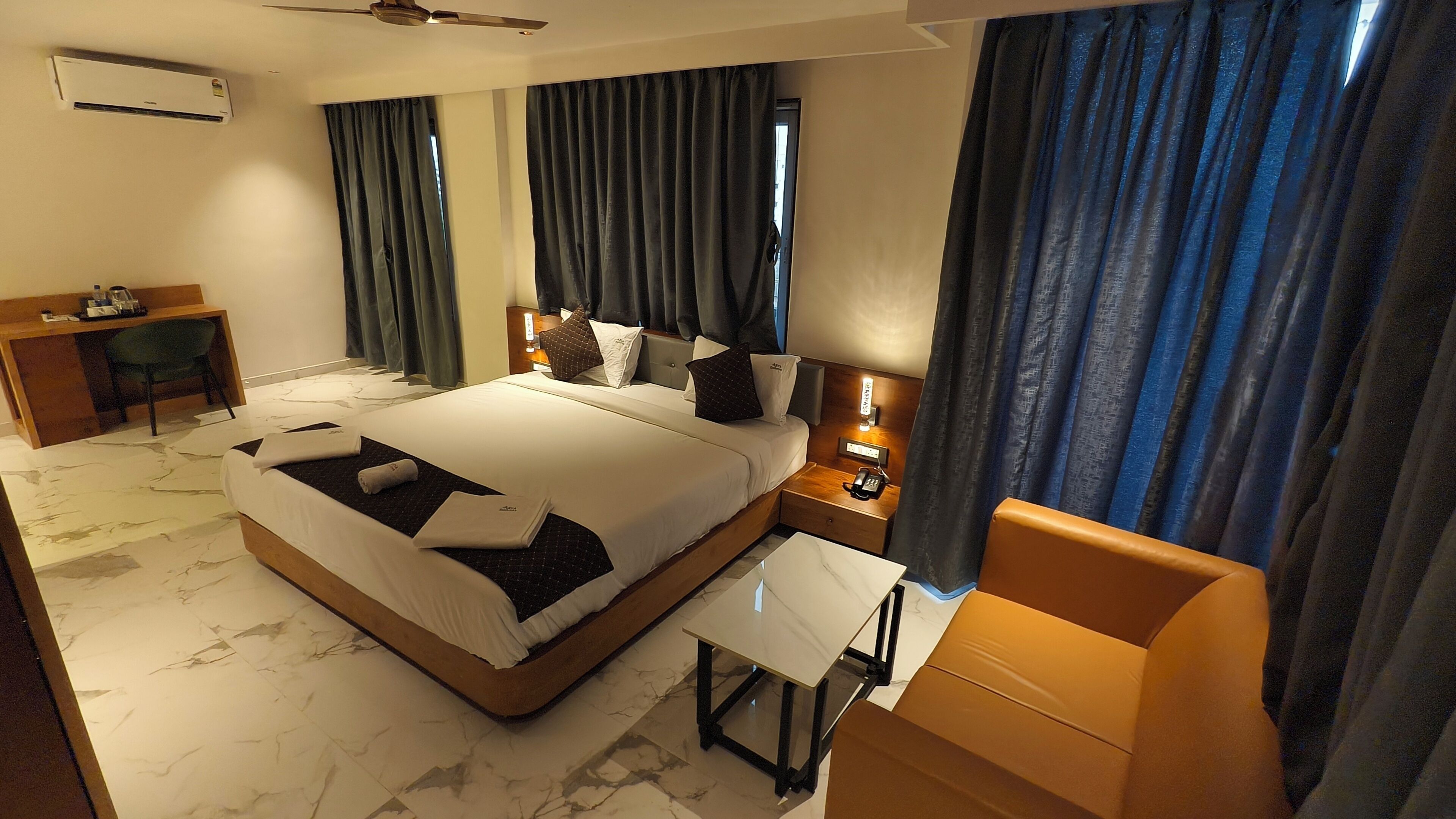A hotel room with a bed, bedside table, lamp, desk, chair, and curtains.