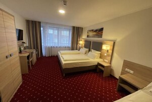 Habitación de hotel con cama, mesitas de noche, escritorio, televisor y ventana con cortinas.