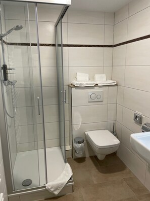 A modern bathroom with a glass-enclosed shower, a toilet, and a sink. - Hotel Harburger Hof (Hamburg)