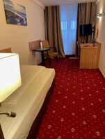 Ein Hotelzimmer mit Bett, Schreibtisch, Stuhl, Fernseher und einem Fenster mit Vorhängen.