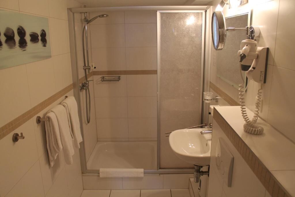A bathroom with a shower, a sink, and a hairdryer mounted on the wall.