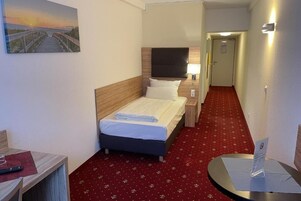 Een hotelkamer met een bed, een bureau, een stoel, een nachtkastje, een lamp en een schilderij aan de muur.