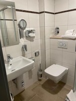Ein Badezimmer mit Waschbecken, Toilette und Spiegel. Ein Handtuchhalter und ein Händetrockner sind vorhanden.