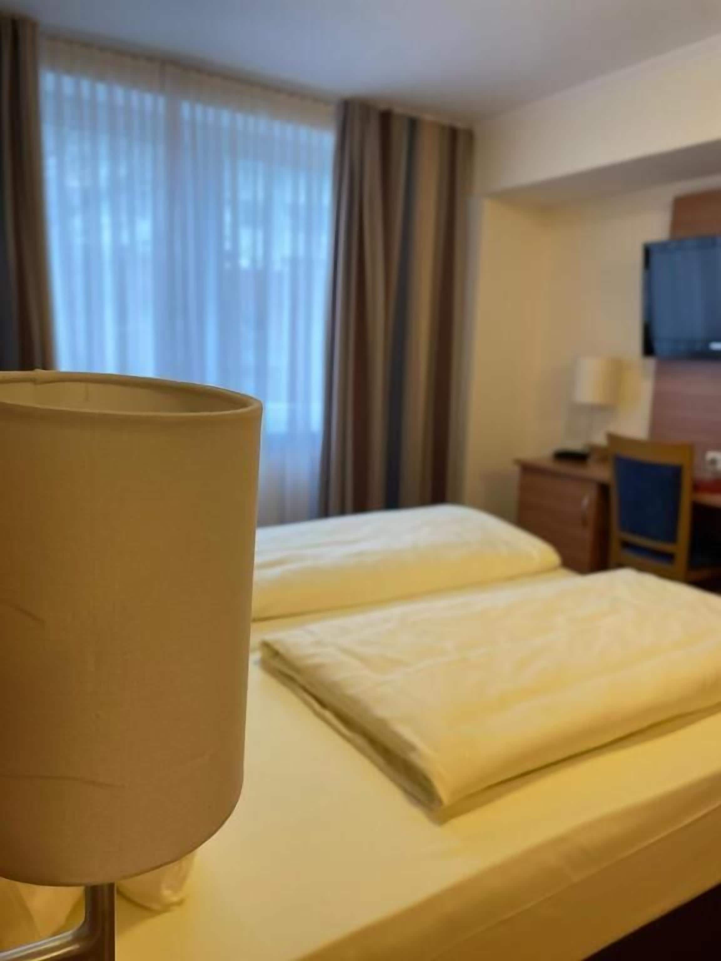 A hotel room with a bed, a lamp, a television, and curtains.