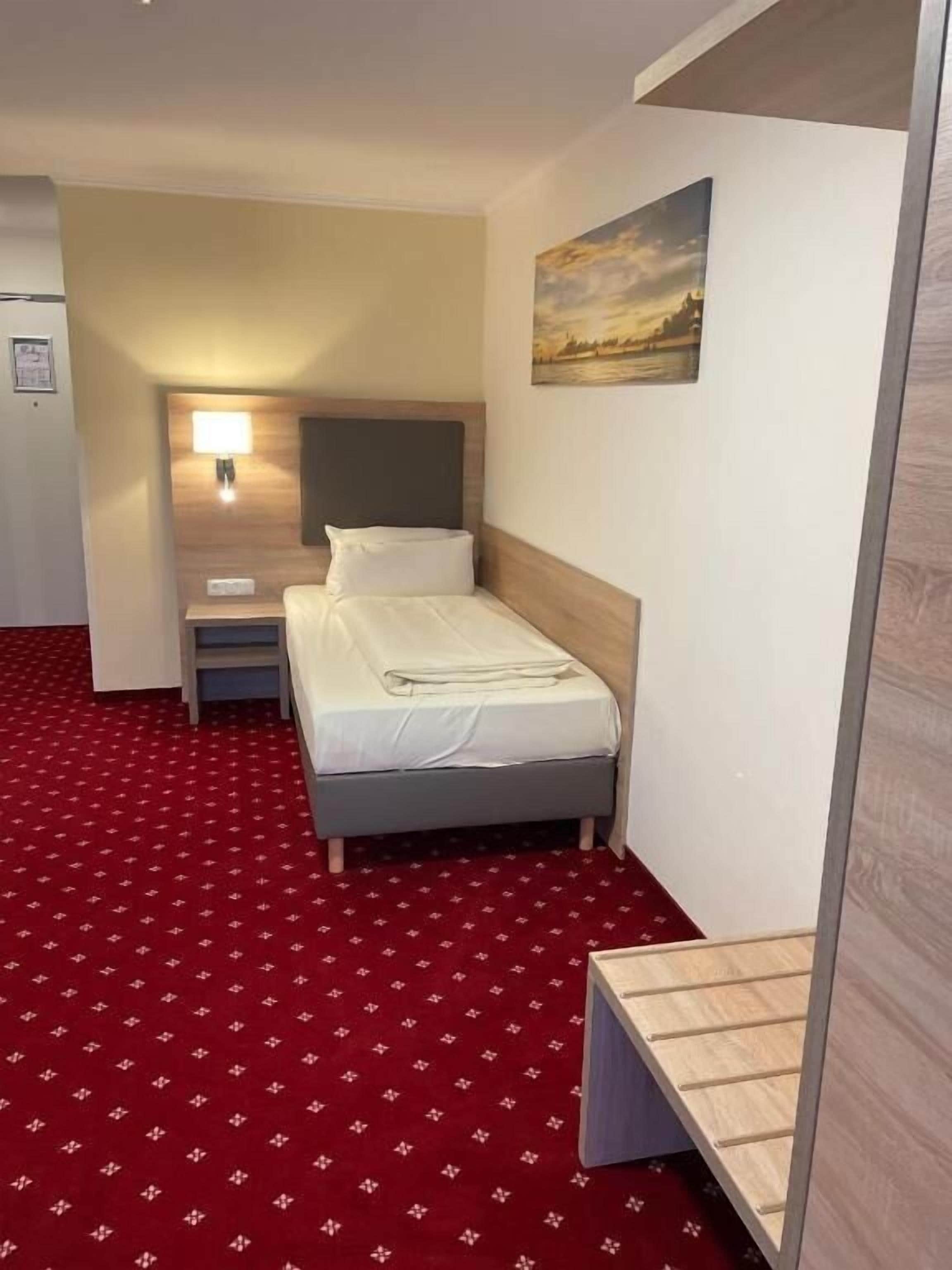 Habitació d'hotel amb un llit, una tauleta de nit, una làmpada i un quadre a la paret.