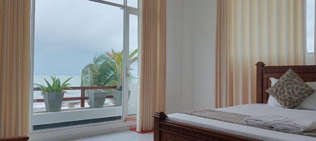 A bedroom with a bed, curtains, and a view of the sea through a window.