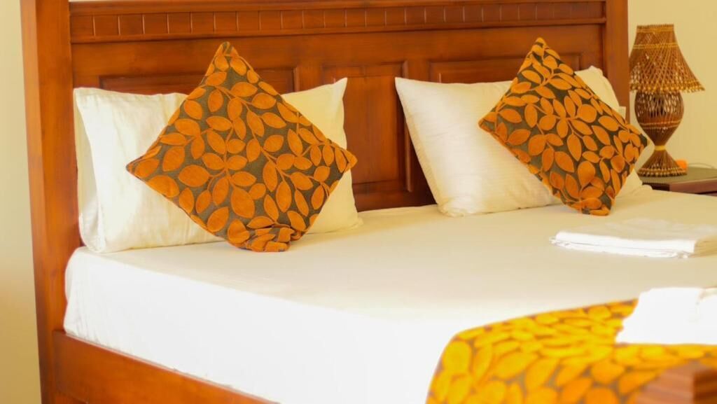 Un lit avec une tête de lit en bois, deux oreillers ornés d’un motif de feuilles et une lampe de chevet.
