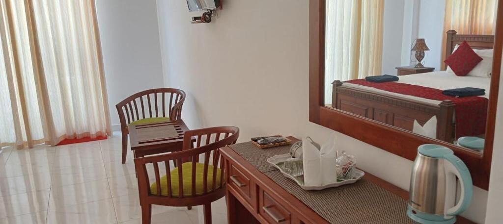 Habitación de hotel con escritorio de madera, sillas, un espejo grande, una cama con almohada roja y un hervidor.