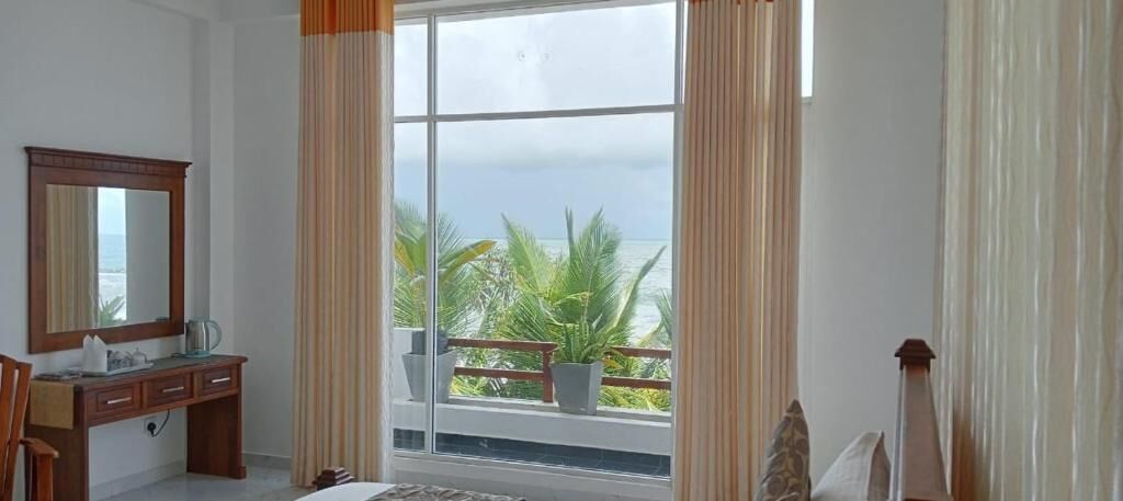 A room with a large window, a wooden desk, a mirror, and a view of the ocean.