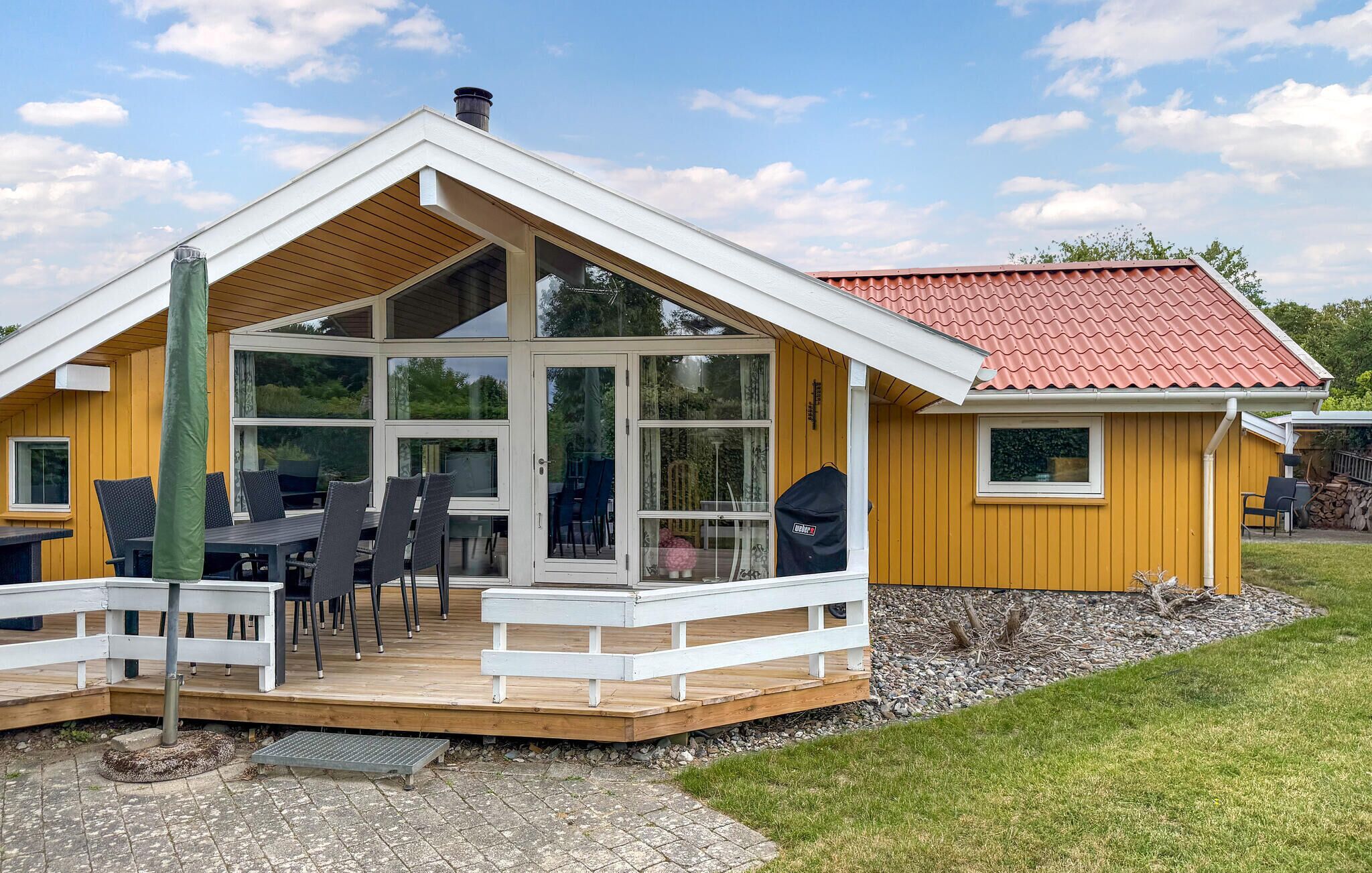 Eine Holzhütte mit einer Terrasse, großen Fenstern und einem roten Ziegeldach.