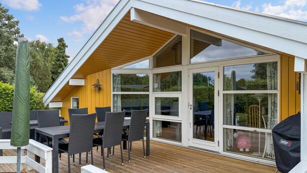 A covered outdoor deck with a dining area, including tables and chairs, and a large sliding glass door leading to an interior space. - Gorgeous home in Nysted with WiFi (Nysted)
