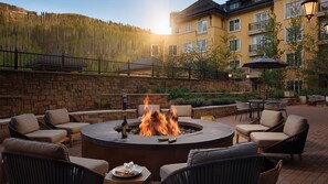 A circular fire pit surrounded by wicker chairs and a table, with a building in the background. - The Ritz-Carlton Club -- 2 bedroom -- Vail, Colorado (Vail)