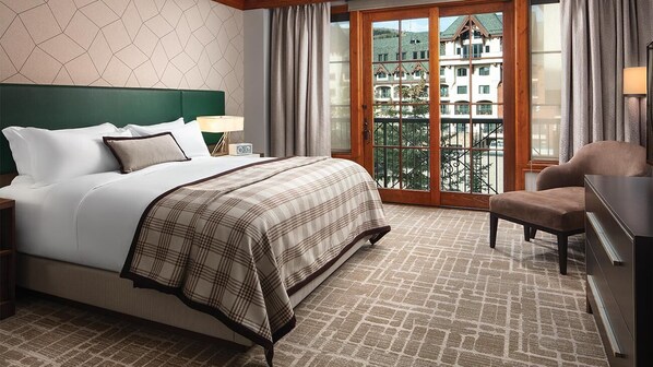 Habitación de hotel con una cama grande, una mesita de noche, una silla, un aparador y un balcón con vistas a edificios.