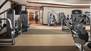 Ett gym med olika träningsmaskiner, ett golv täckt med matta och trädetaljer.