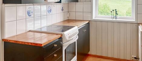A kitchen with a stove, oven, and cabinets, a window with a view of greenery, and a tiled backsplash.