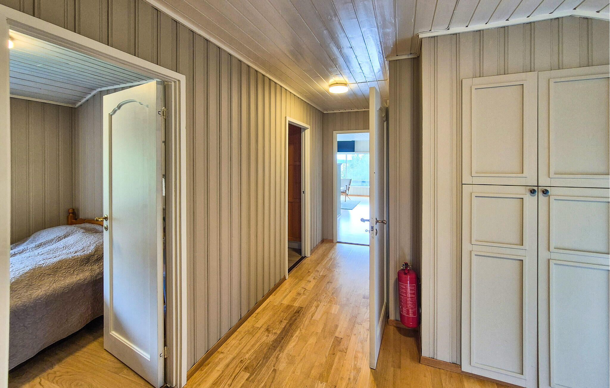 Un corridoio con pavimento in legno, un letto, un estintore e una porta che dà su un balcone.