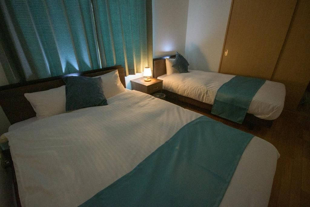 A hotel room with two beds, a nightstand with a lamp, and a window with curtains.