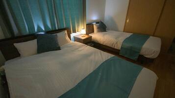 A hotel room with two beds, a nightstand with a lamp, and a window with curtains.