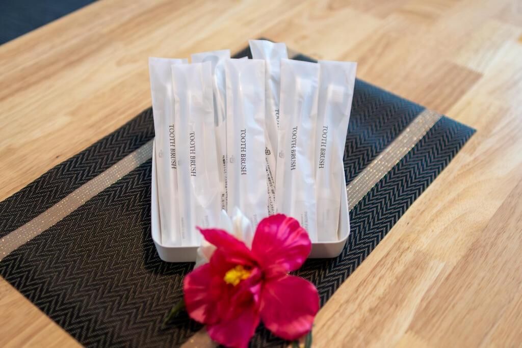 Un juego de cepillos de dientes blancos en un recipiente con una flor rosa sobre una mesa estampada.
