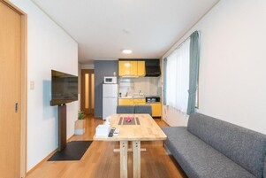 A compact living space with a kitchenette, a sofa, a dining table, and a TV.
