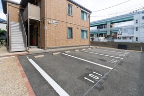 Un estacionamiento con espacios delimitados, un edificio de fachada de ladrillo y una escalera que lleva a una puerta.