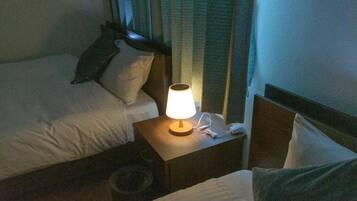A hotel room with two beds, a nightstand with a lamp, and a telephone.