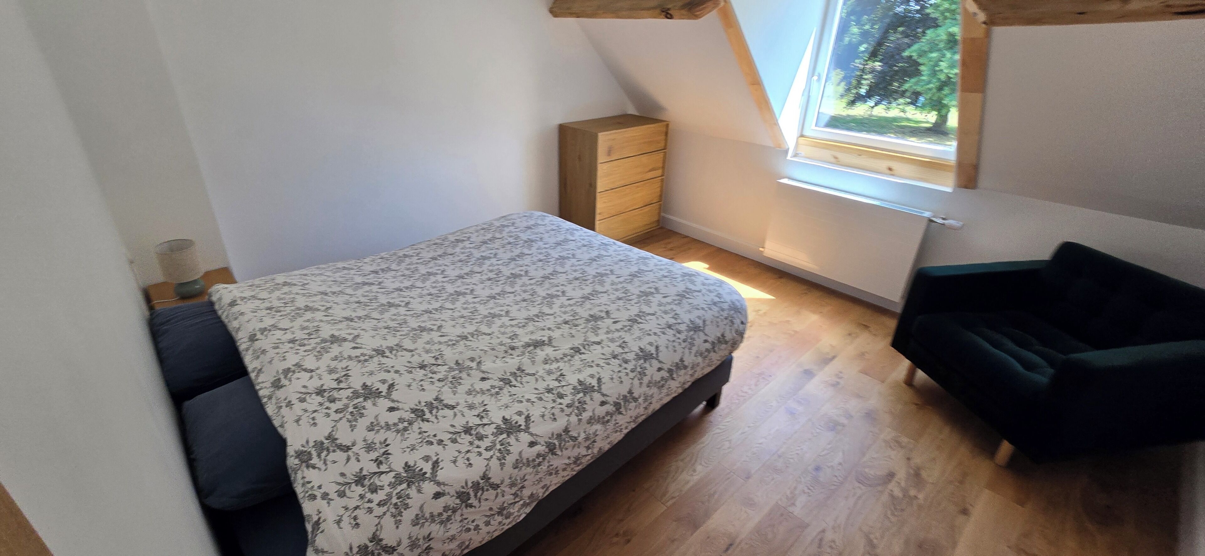 Ein Schlafzimmer mit einem Bett, einem Schminktisch, einem Fenster und einem dunkel gefärbten Stuhl.
