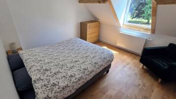 Een slaapkamer met een bed, een dressoir, een raam en een donkere stoel.