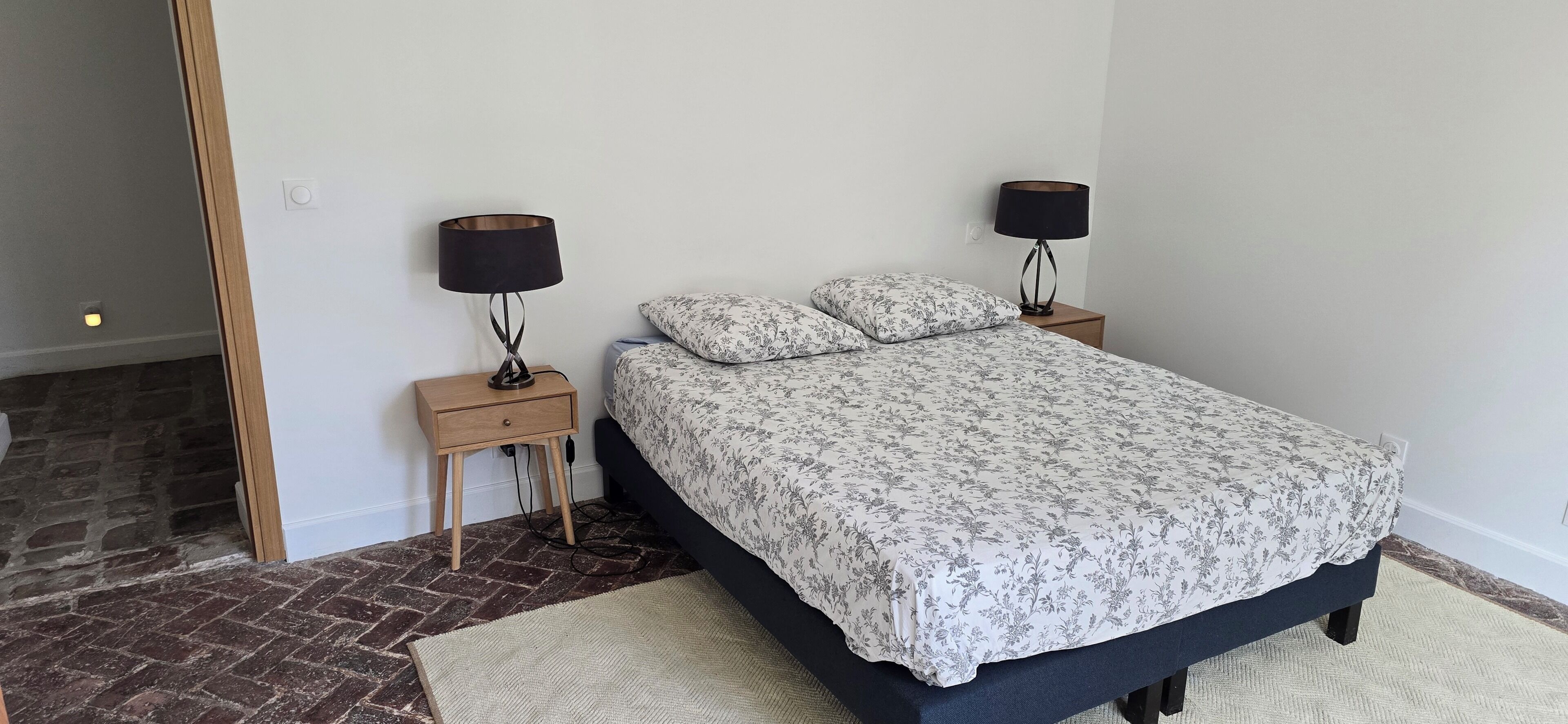 A bedroom with a bed, two bedside tables, two lamps, and a rug.