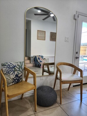 A room with a large mirror, two wooden chairs, a round ottoman, and a door leading outside. - Pool house 3 bedroom 2 bath pool house (Galveston)