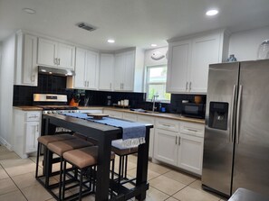 A modern kitchen with white cabinets, a stainless steel refrigerator, and a bar area with stools. - Pool house 3 bedroom 2 bath pool house (Galveston)