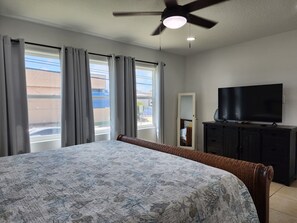 A hotel room with a bed, a television, a ceiling fan, and a window with curtains. - Pool house 3 bedroom 2 bath pool house (Galveston)