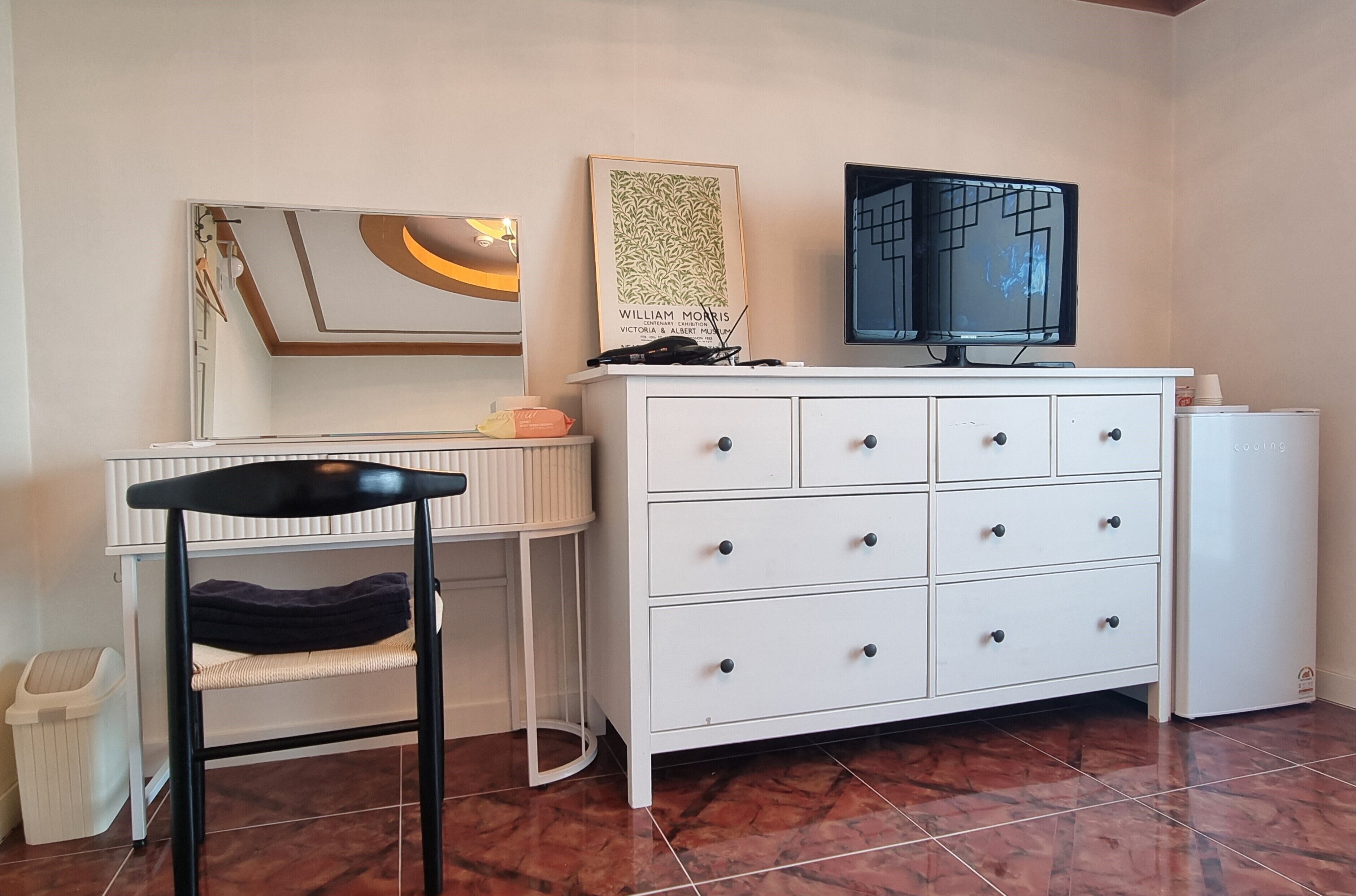 A room with a white dresser, a chair, a television, and a framed picture on the wall.