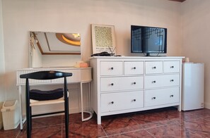 A room with a white dresser, a chair, a television, and a framed picture on the wall.