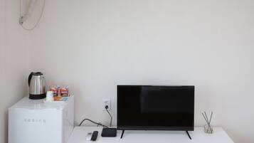 A room with a white entertainment unit, a flat-screen TV, a small refrigerator, and an air conditioning unit mounted on the wall.
