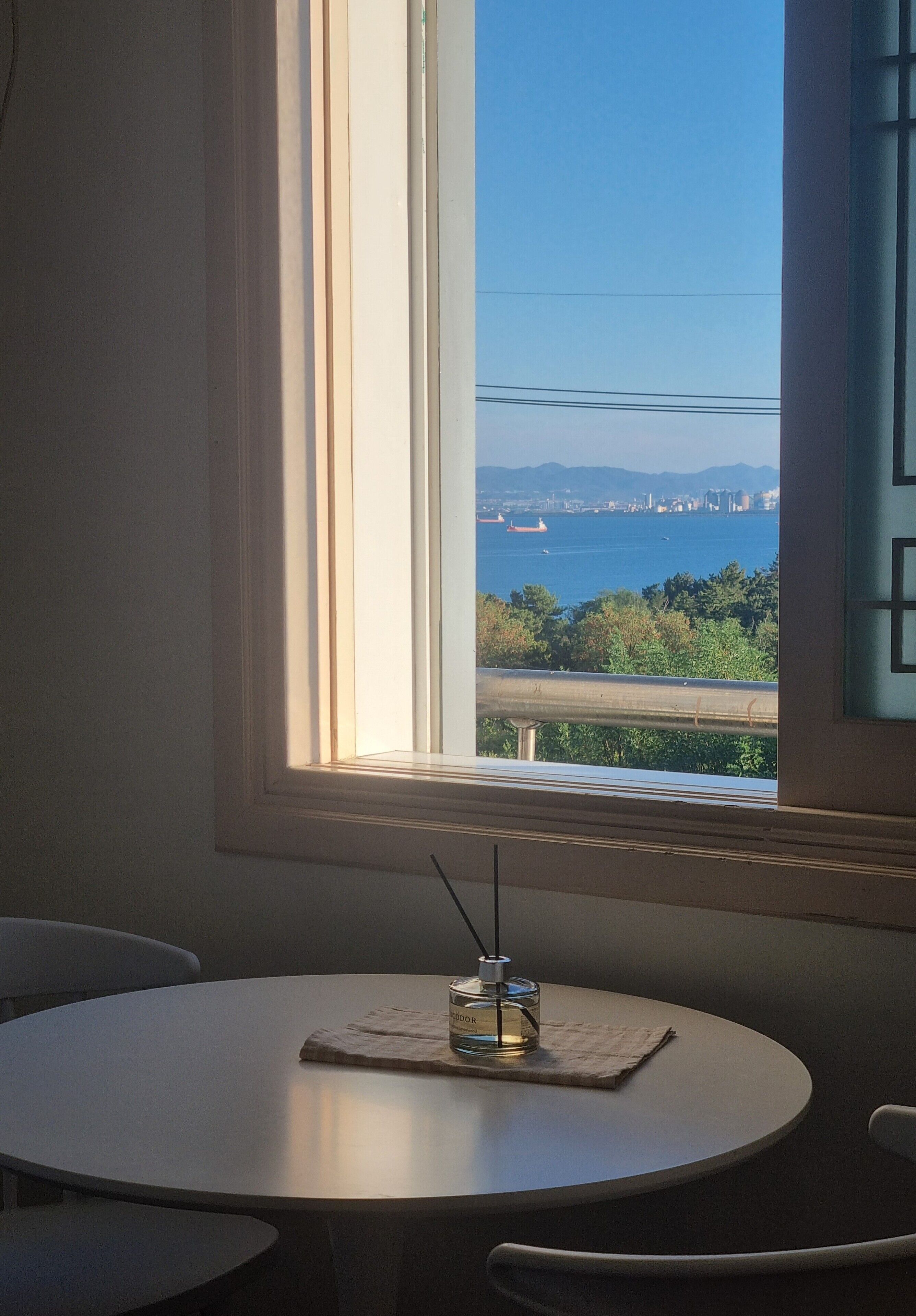 Una mesa con una botella de perfume y una servilleta, una ventana que ofrece vistas a un cuerpo de agua y tierra a lo lejos.