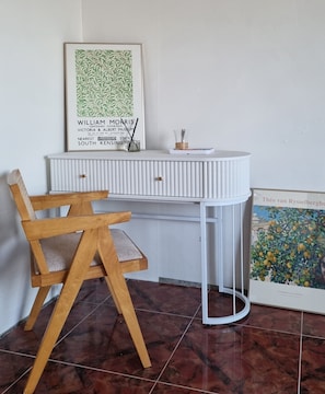 A corner desk with a framed artwork above it, a small table with a candle, and a chair with a cushion. - Gloriastay (Pohang)
