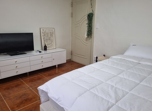 A bedroom with a bed, a TV on a white dresser, and a door with a decorative hanging.