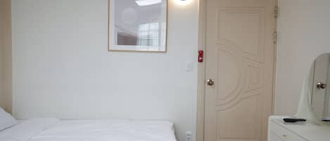 A bedroom with a bed, a dresser, a mirror, a door, and a wall-mounted light fixture.
