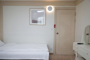 A bedroom with a bed, a dresser, a mirror, a door, and a wall-mounted light fixture. - Gloriastay (Pohang)