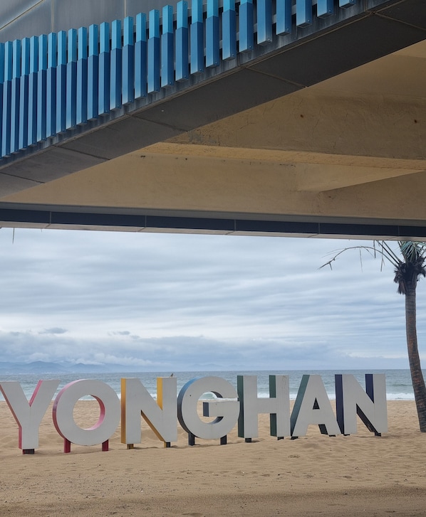 Grandes letras que dicen 'YONGHAN' en una playa con una palmera y el océano al fondo.