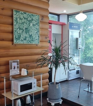 A modern interior with a wooden wall, a potted plant, a microwave, and a vending machine.