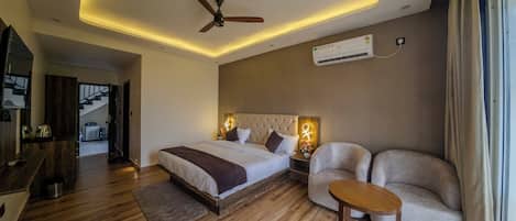 Un dormitorio con cama, ventilador de techo, aire acondicionado, sofá y una pequeña mesa.