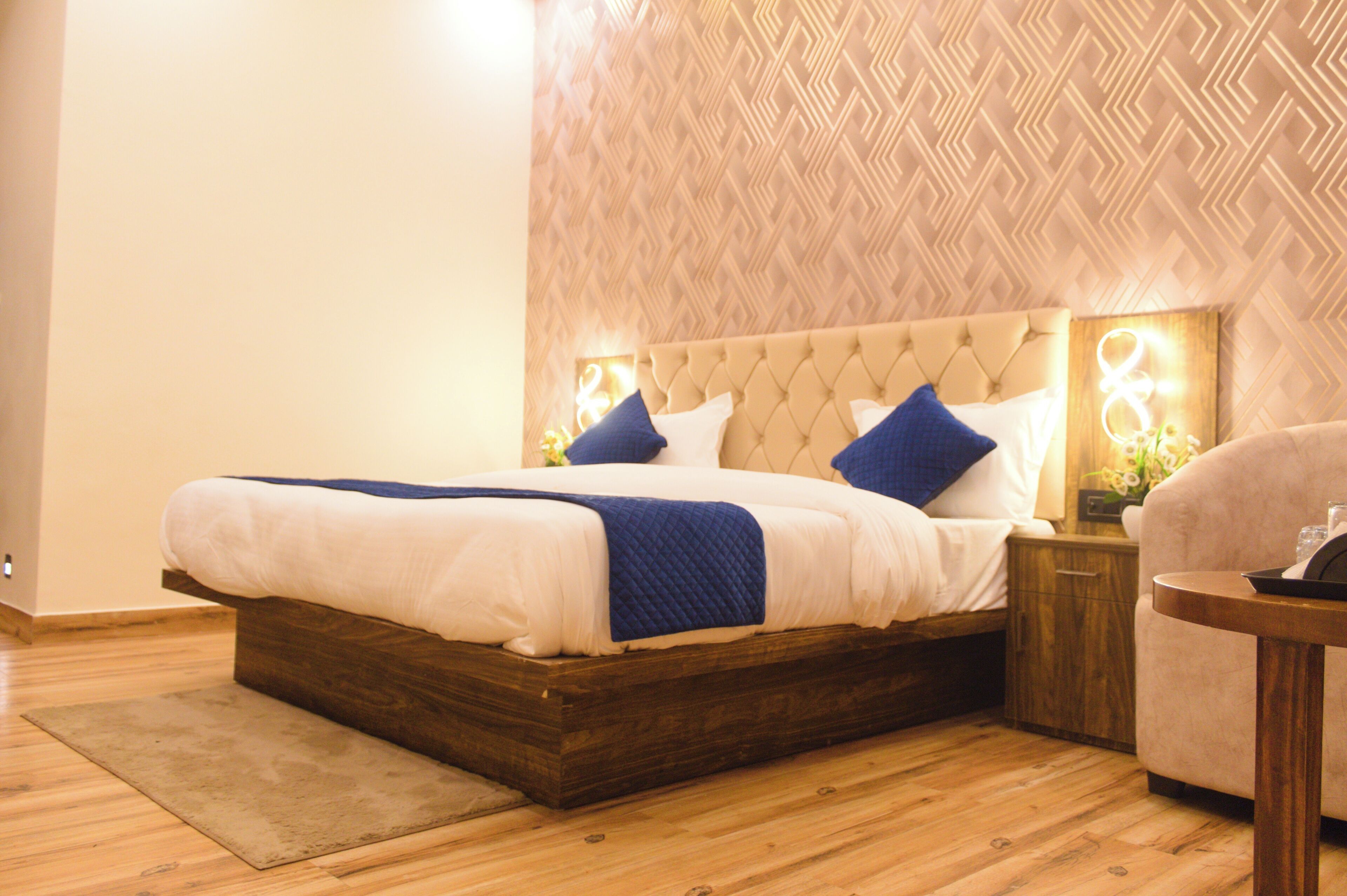 Une chambre d’hôtel avec un grand lit, une tête de lit en bois, une table de chevet avec une lampe et une petite table ronde.