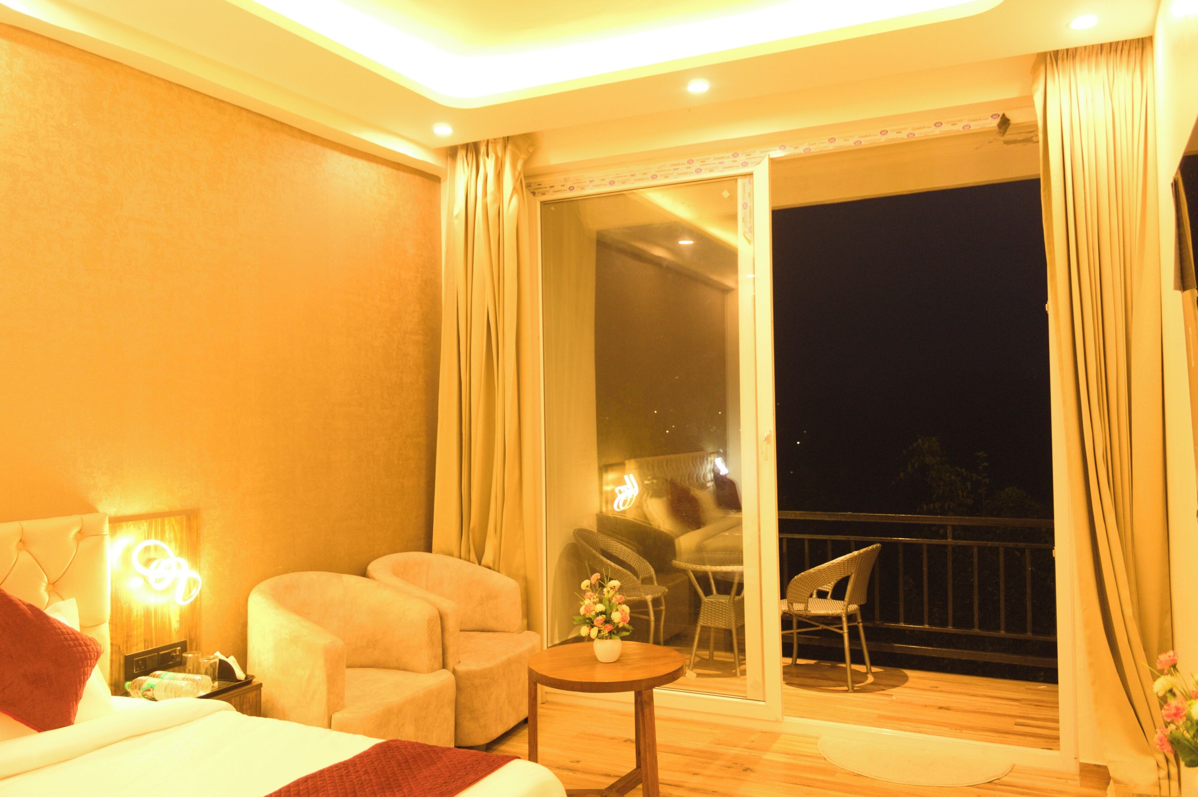 A hotel room with a bed, two armchairs, a small table with a vase of flowers, and a balcony with a chair.