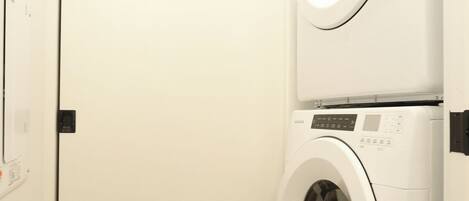 A laundry room with two stacked front-loading washing machines and a door with a light switch.
